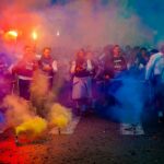 A lively group celebrating at night with color smoke bombs in a street festival.